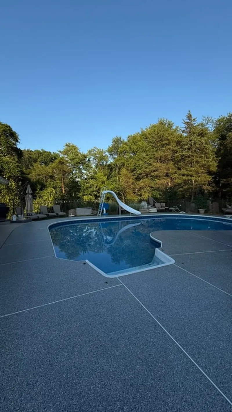 Wide view of finished pool deck coated with Simiron Tidal Wave Stonewash flake system with expansion joint lines and water slide in Hillsborough Township, NJ